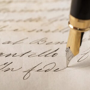 Puede incluir: Primer plano de una pluma estilogr&aacute;fica con plum&iacute;n dorado escribiendo sobre papel envejecido. La pluma es negra con detalles dorados. El papel presenta escritura manuscrita en tinta negra, con cursiva elegante.