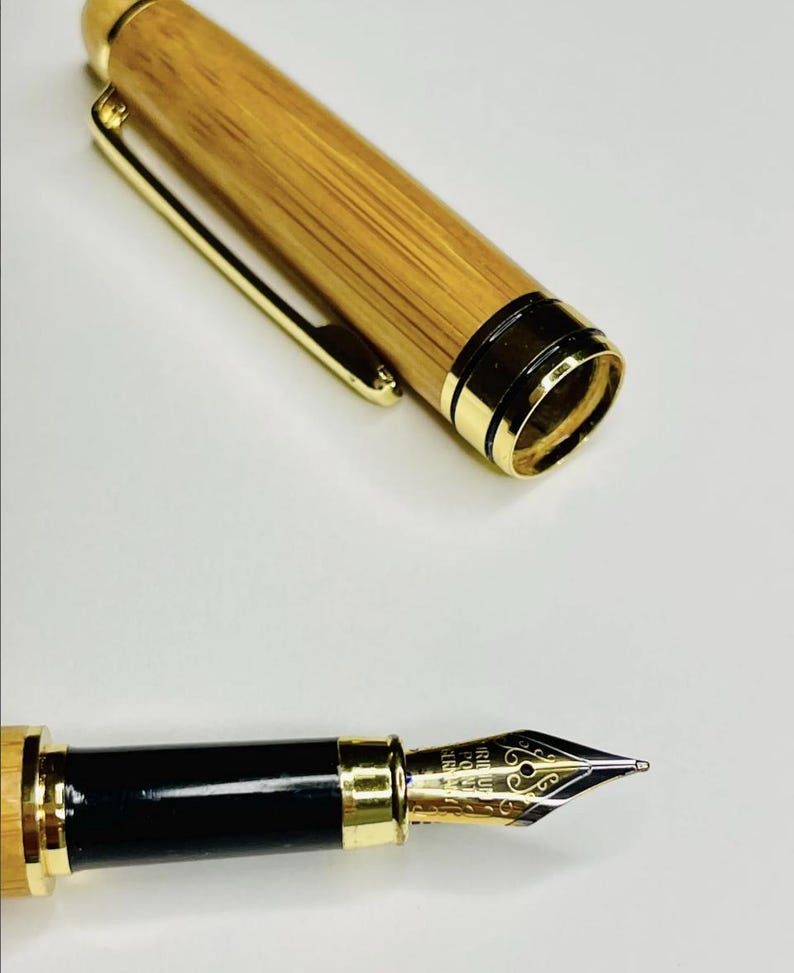 Puede incluir: Una pluma estilogr&aacute;fica con un cuerpo de bamb&uacute; y detalles dorados. La tapa de la pluma est&aacute; quitada, revelando el plum&iacute;n. El plum&iacute;n es dorado con dise&ntilde;os intrincados. La pluma tiene una secci&oacute;n de agarre negra.