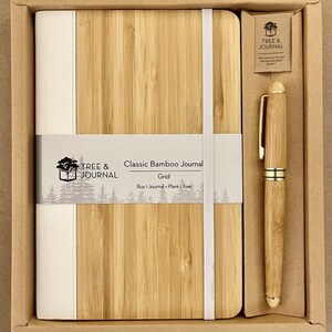 Puede incluir: Un juego de diario y bol&iacute;grafo de bamb&uacute; en una caja de cart&oacute;n. El diario es de color marr&oacute;n claro con una lomo y banda el&aacute;stica blancos. El bol&iacute;grafo tambi&eacute;n es de color bamb&uacute; con detalles dorados. El texto del diario dice "Classic Bamboo Journal".