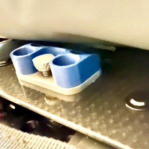 May include: A blue plastic 3D printed object with a silver knob. The object has three holes and is attached to a silver surface.