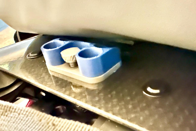 May include: A blue plastic 3D printed object with a silver knob. The object has three holes and is attached to a silver surface.