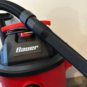 May include: A red and black wet/dry vacuum with a black hose and a black crevice tool. The vacuum has the word "Bauer" printed on the side.