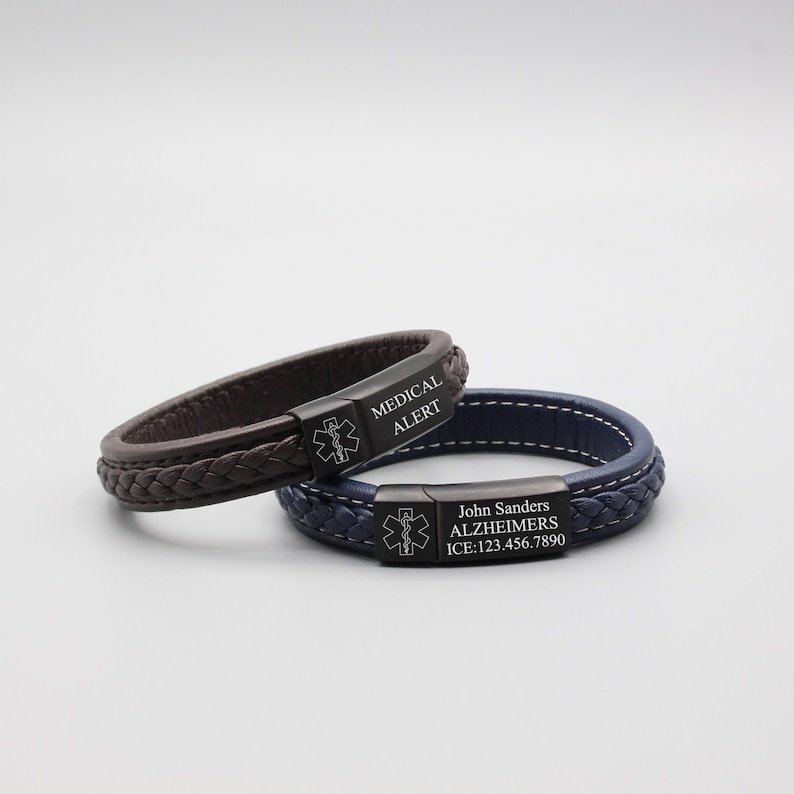 May include: Two leather bracelets with black metal medical alert tags. The top bracelet is brown with the text "MEDICAL ALERT". The bottom bracelet is blue with the text "John Sanders ALZHEIMERS ICE: 123.456.7890".