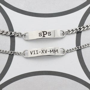 May include: Two silver bracelets with engraved rectangular tags. The top tag reads "sPs" and the bottom tag reads "VII-XV-MM".