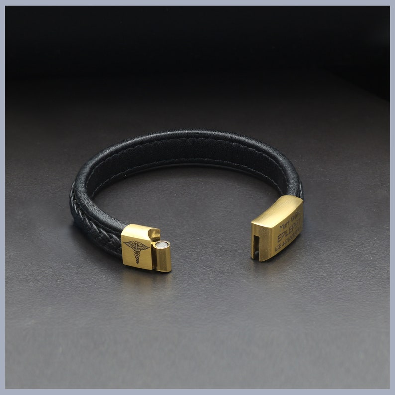 May include: Black leather bracelet with a gold-toned clasp. The clasp features a medical symbol and the text "Medical Alert Epilepsy 911".