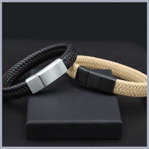 May include: Two braided leather bracelets with metal clasps. One bracelet is brown and the other is beige.