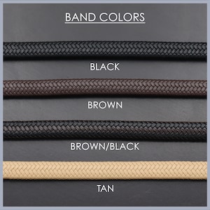 May include: Four braided watch bands in different colors: black, brown, brown/black, and tan. The bands are displayed on a gray background with the text "BAND COLORS" at the top and the color names below each band.