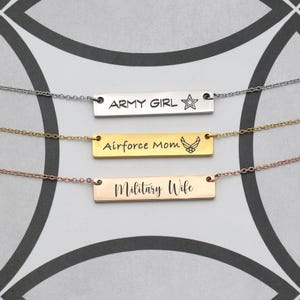 Op de afbeelding: Drie kettingen met rechthoekige hangers. De bovenste ketting is zilverkleurig met "ARMY GIRL" en een ster. De middelste ketting is goudkleurig met "Airforce Mom" en een embleem. De onderste ketting is roségoudkleurig met "Military Wife".