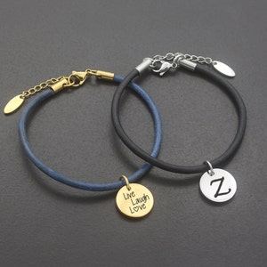 May include: Two leather bracelets with charms. One bracelet is black with a silver charm that says "Z". The other bracelet is blue with a gold charm that says "Live Laugh Love" with a heart symbol.