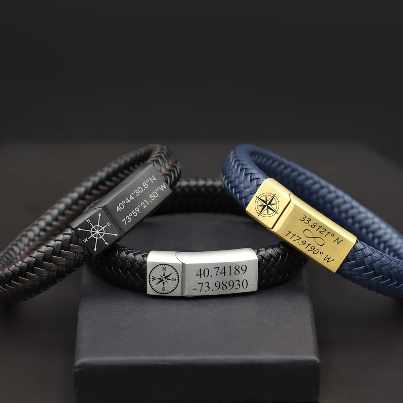 May include: Three leather bracelets with compass charms and engraved coordinates. The bracelets are black, brown, and blue. The coordinates are 40&deg;44'30.8"N 73&deg;59'21.50"W, 40.74189 -73.98930, and 33.8121&deg; N 117.9190&deg; W.