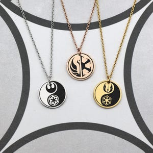 Puede incluir: Tres collares con cadenas. Los colgantes redondos presentan varios diseños en blanco y negro o dorados. Un colgante tiene un diseño de yin-yang con un símbolo, otro tiene un símbolo y el tercero tiene un símbolo.