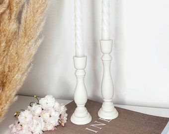 May include: Two white candlesticks with white twisted candles on top. The candlesticks are on a brown book with the word "LINE" visible. The candlesticks are on a white surface.
