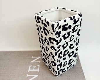 May include: A white ceramic square vase with a black leopard print design.