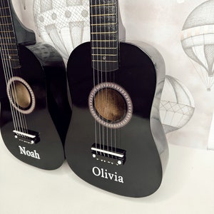 May include: Two black acoustic guitars with strings, one with the name "Noah" and the other with the name "Olivia" written on the body.