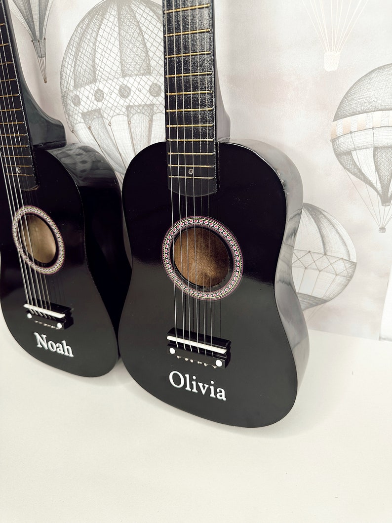 May include: Two black acoustic guitars with strings, one with the name "Noah" and the other with the name "Olivia" written on the body.