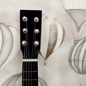 May include: Close-up of the headstock of a black acoustic guitar with six strings and silver tuning pegs.