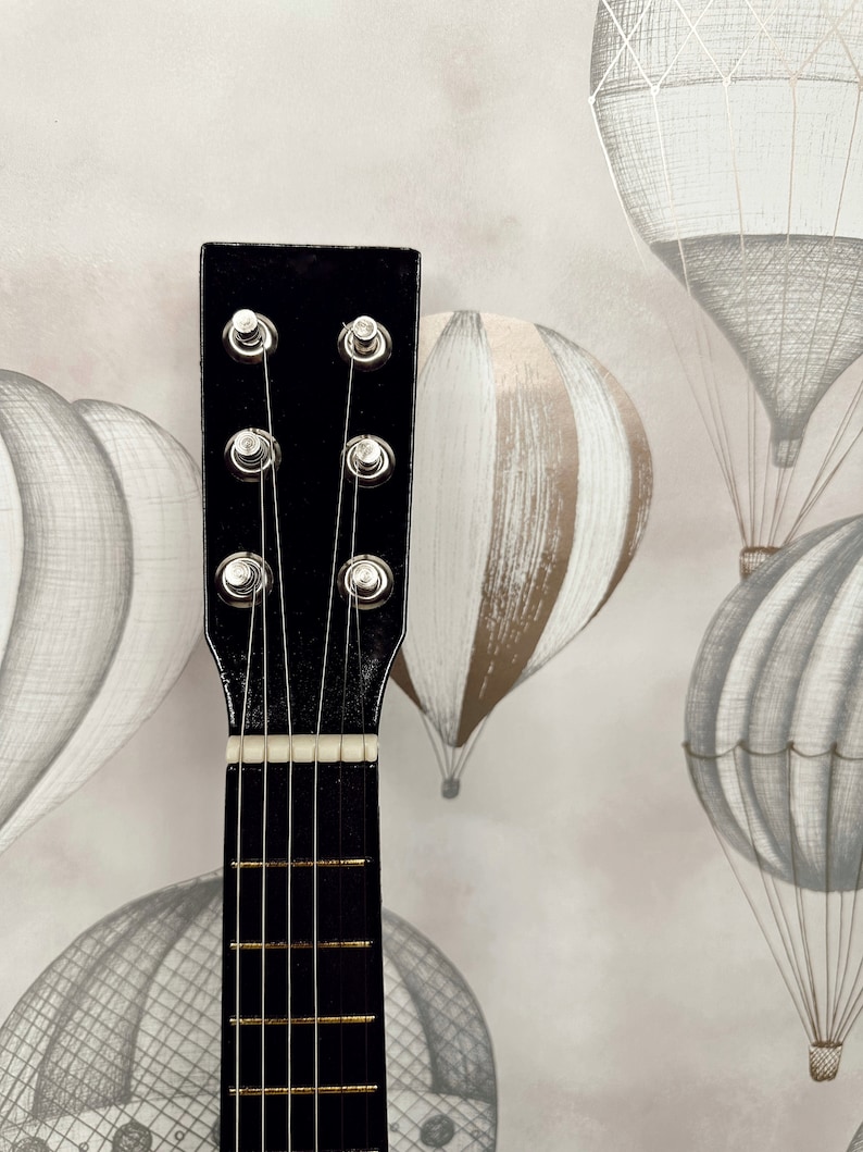 May include: Close-up of the headstock of a black acoustic guitar with six strings and silver tuning pegs.