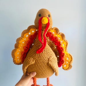 May include: A handmade crochet turkey with brown, orange, and red details. The turkey has a yellow wattle and a red snood. The wings are a mix of orange, yellow, and red. The turkey is a festive decoration.