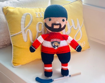 May include: A handmade crochet hockey player doll wearing a red, white, and blue jersey with the Florida Panthers logo. The doll has a black hat, beard, and a hockey stick. The doll is approximately 8 inches tall.