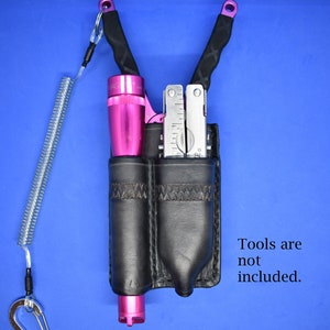 May include: A black leather double holster with a pink flashlight and a multi-tool. Tools are not included.