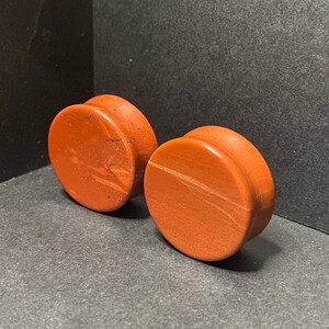 May include: Two round, brown wood ear gauges. The gauges have a natural wood grain pattern.