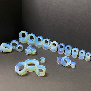 Könnte beinhalten: Eine Sammlung von Opalit-Ohrenstretchern in verschiedenen Größen, von klein bis groß. Die Stretcher sind hellblau mit einem durchscheinenden Finish.