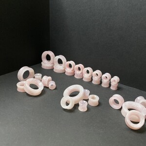 May include: A set of pink rose quartz ear gauges in various sizes. The gauges are made from natural stone and have a smooth, polished finish.