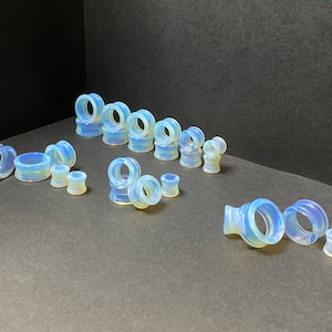 May include: A set of 18 opal glass ear gauges in various sizes. The gauges are a light blue color with a swirling pattern.