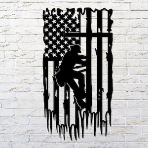 May include: Black metal silhouette of a lineman climbing a utility pole, superimposed on an American flag with a distressed, dripping effect.