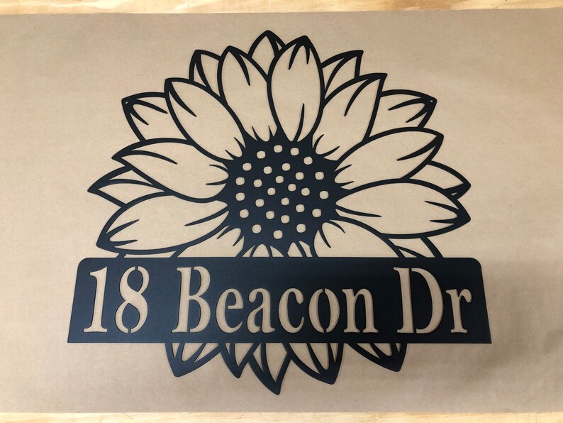 Op de afbeelding: Zwarte metalen zonnebloemdecoratie met een zwart metalen bord met de tekst "18 Beacon Dr".
