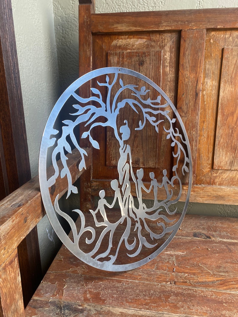 May include: A metal wall art piece depicting a tree of life with intricate branches and leaves.  The tree is surrounded by a circle and has several figures standing at the base of the tree.