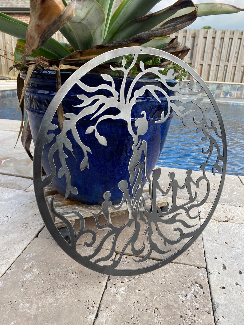 May include: A metal wall art piece depicting a tree of life with intricate branches and roots. Five figures are holding hands, symbolising family and unity. The artwork is circular and has a rustic, weathered finish.