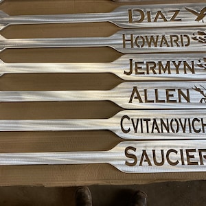 May include: Six silver metal paddles with names and animal silhouettes cut out. The names are Diaz, Howard, Jermyn, Allen, Cvitanovich, and Saucier.