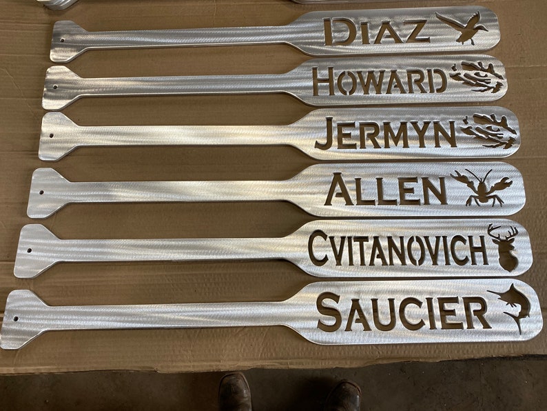 May include: Six silver metal paddles with names and animal silhouettes cut out. The names are Diaz, Howard, Jermyn, Allen, Cvitanovich, and Saucier.