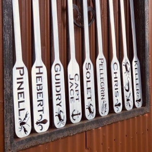 May include: Nine silver paddles with various names engraved on them, including "Pinell", "Hebert", "Guidry", "Jace", "Capt", "Solet", "Pellegrin", "Chris", and "Keller".