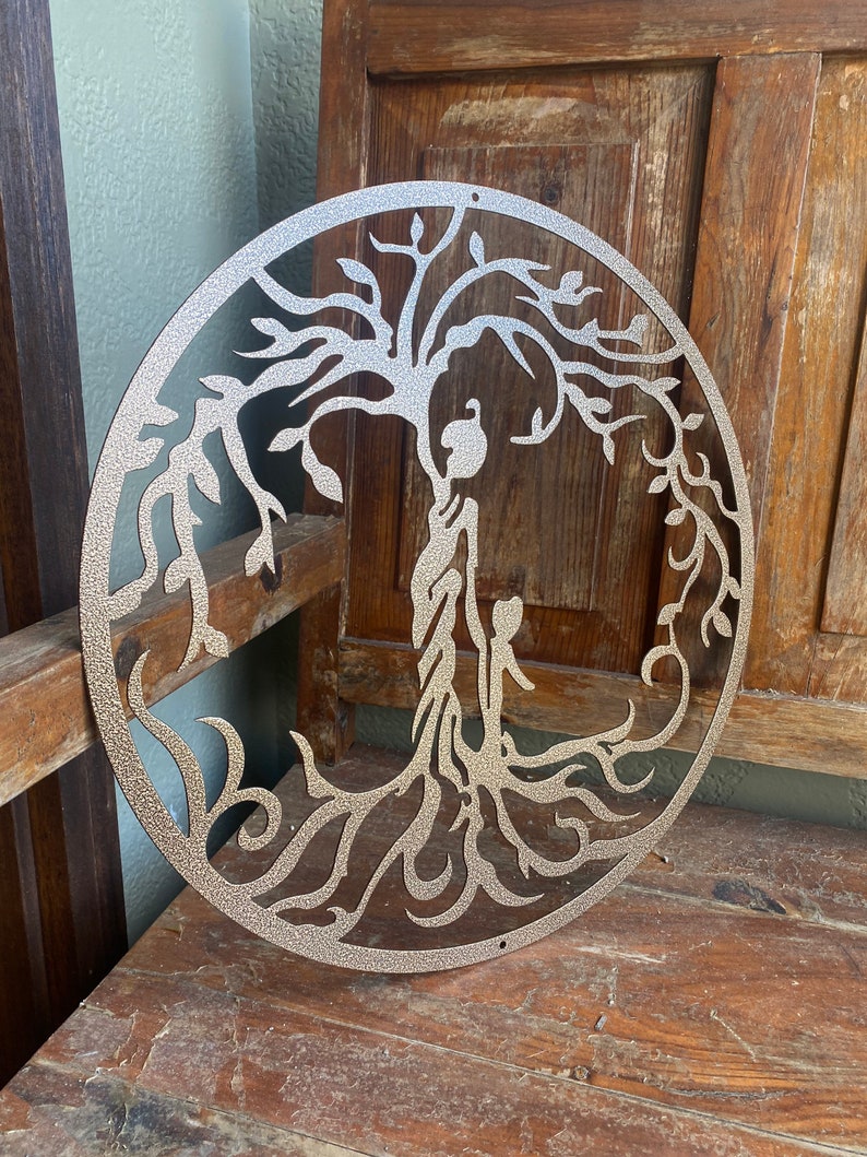 May include: A silver metal tree of life wall decoration with intricate branches and roots. The tree is circular and has a textured surface.