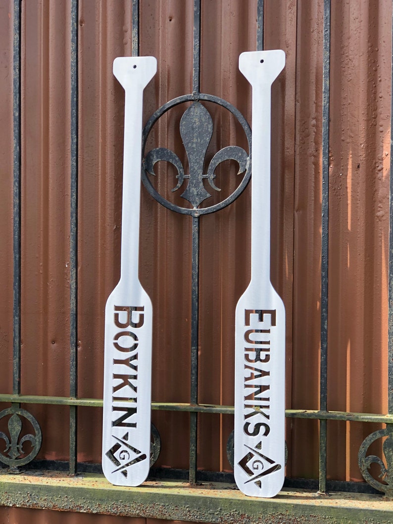 May include: Two white wooden paddles with the names "Boykin" and "Eubanks" cut out in the wood. Each paddle has a small square and compass symbol at the bottom.