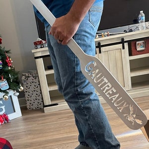May include: A white wooden paddle with the word "GAUTREAUX" carved into it. The paddle has a cutout of a crawfish at the bottom.