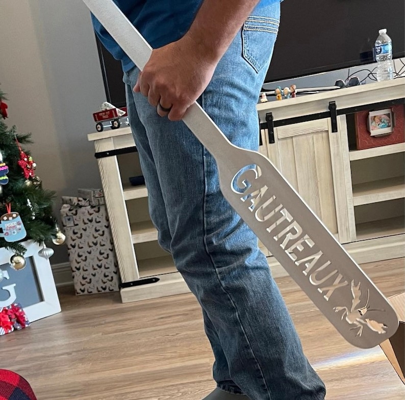 May include: A white wooden paddle with the word "GAUTREAUX" carved into it. The paddle has a cutout of a crawfish at the bottom.