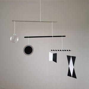 Può includere: Un mobile bianco e nero con forme geometriche e una sfera di vetro appesa a un'asta da soffitto bianca.