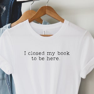 Op de afbeelding: Wit T-shirt met de tekst "Ik heb mijn boek dicht gedaan om hier te zijn."