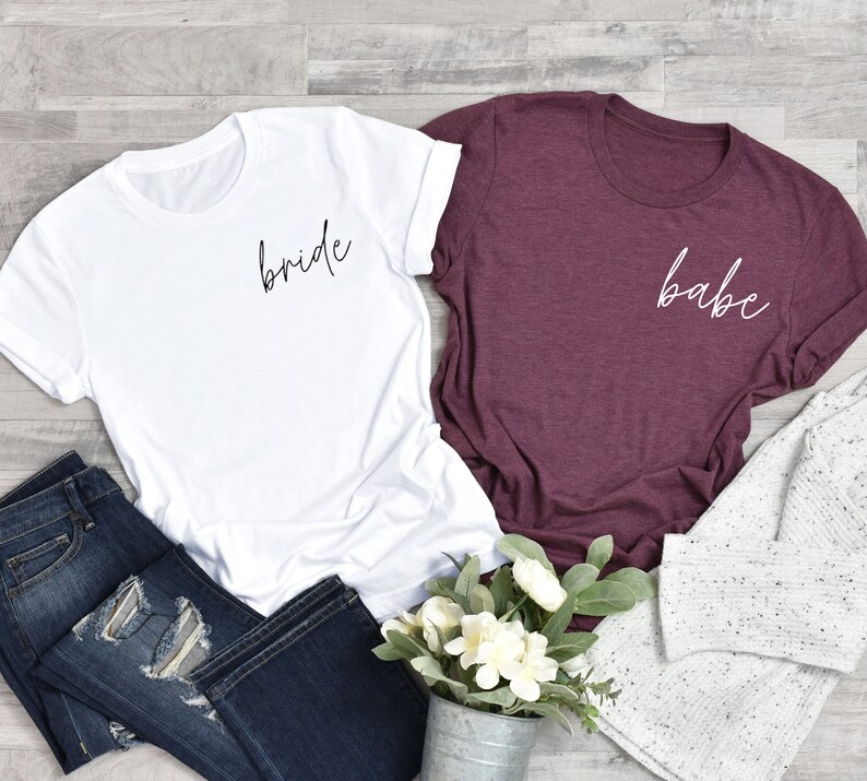 May include: Two t-shirts, one white with the word "bride" in black script and one maroon with the word "babe" in white script.