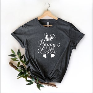 Op de afbeelding: Een donkergrijs T-shirt met een wit konijnenorenontwerp en de tekst "Happy Easter" gedrukt op de voorkant.