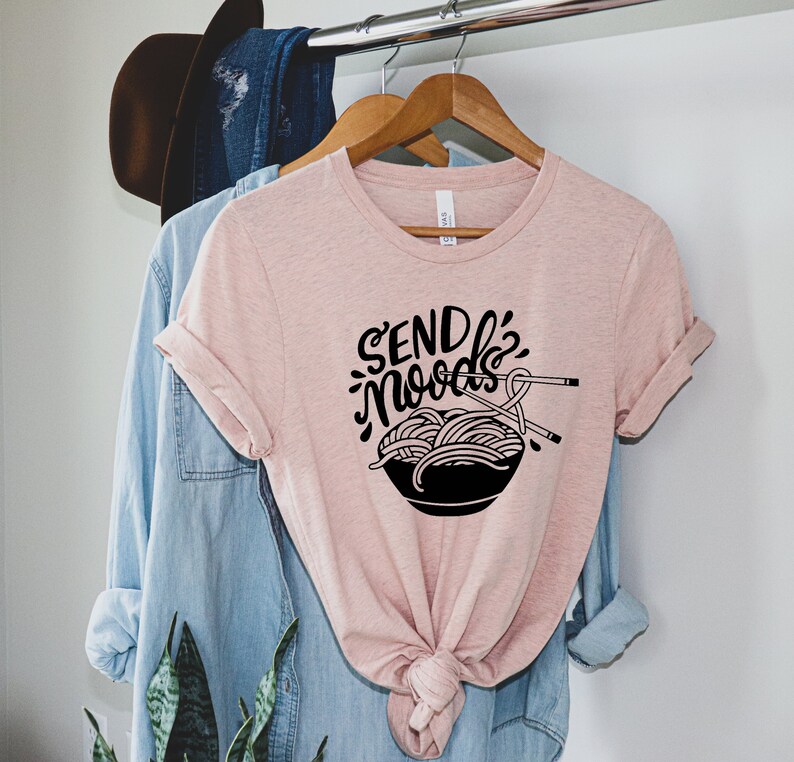 May include: A pink t-shirt with the text "Send Noodles" in black lettering and a black illustration of a bowl of noodles with chopsticks.
