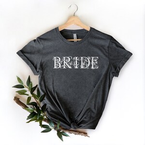 Może przedstawiać: Szary t-shirt z nadrukiem "BRIDE" w kolorze białym z kwiatowymi akcentami.