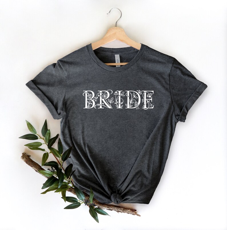 Może przedstawiać: Szary t-shirt z nadrukiem "BRIDE" w kolorze białym z kwiatowymi akcentami.