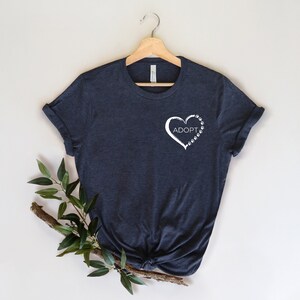 May include: A dark blue t-shirt with a white heart design featuring the word "ADOPT" and paw prints.