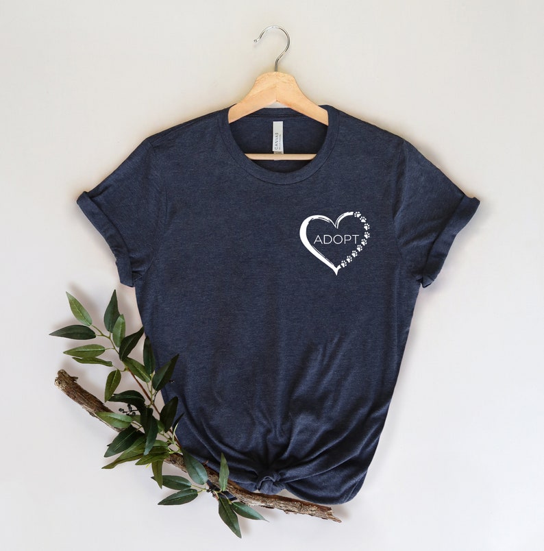 May include: A dark blue t-shirt with a white heart design featuring the word "ADOPT" and paw prints.