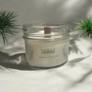 May include: A white candle in a clear glass jar with a wooden wick. The jar has a label that says "Naked - Beeswax - Coconut Wax".