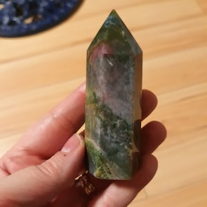 May include: A green, pink and grey crystal point with a pointed top and a flat base.